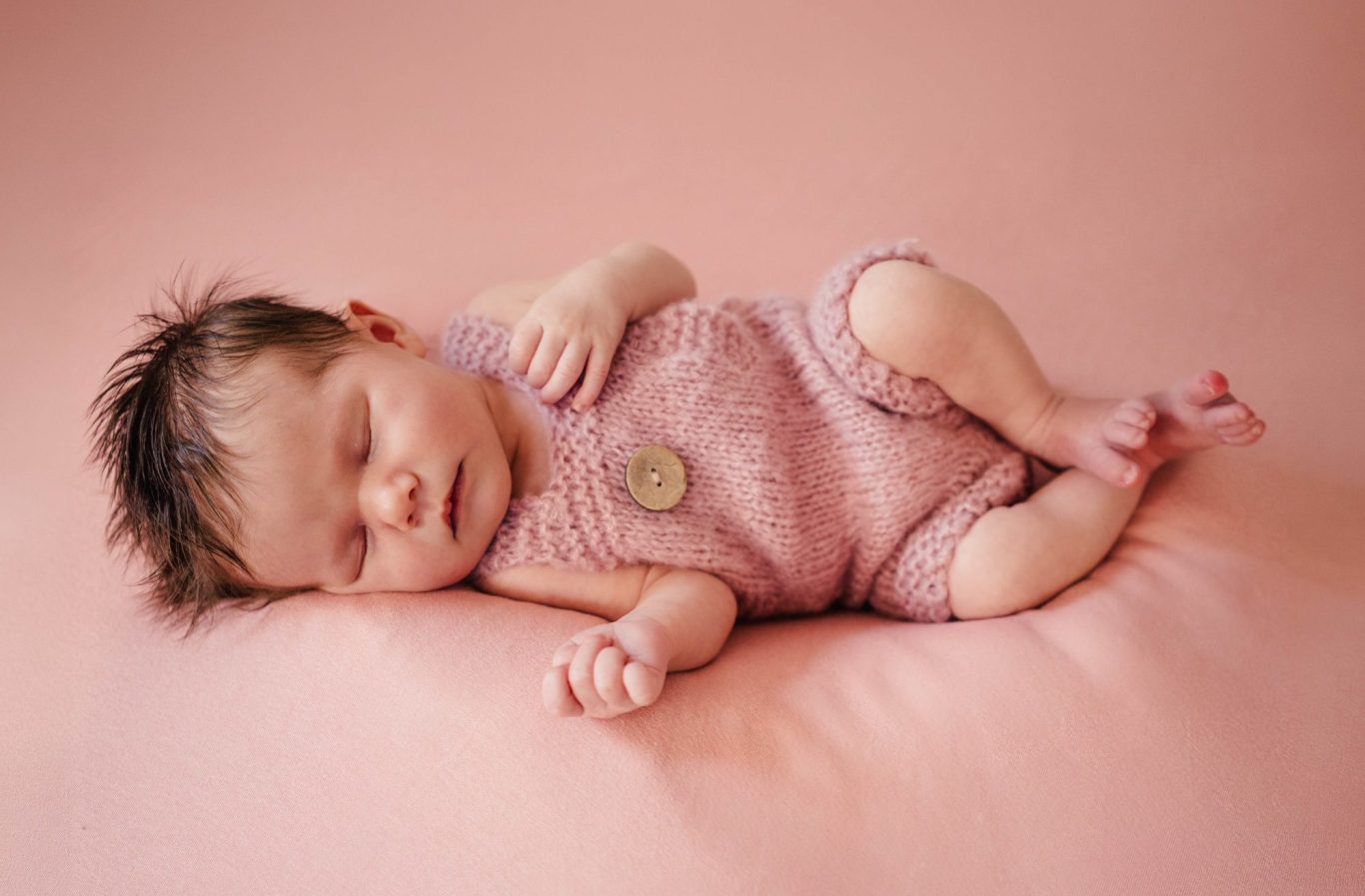 Newbornfotografie Schlafendes Baby in rosafarbenem Strickoutfit auf einem sanften Untergrund.