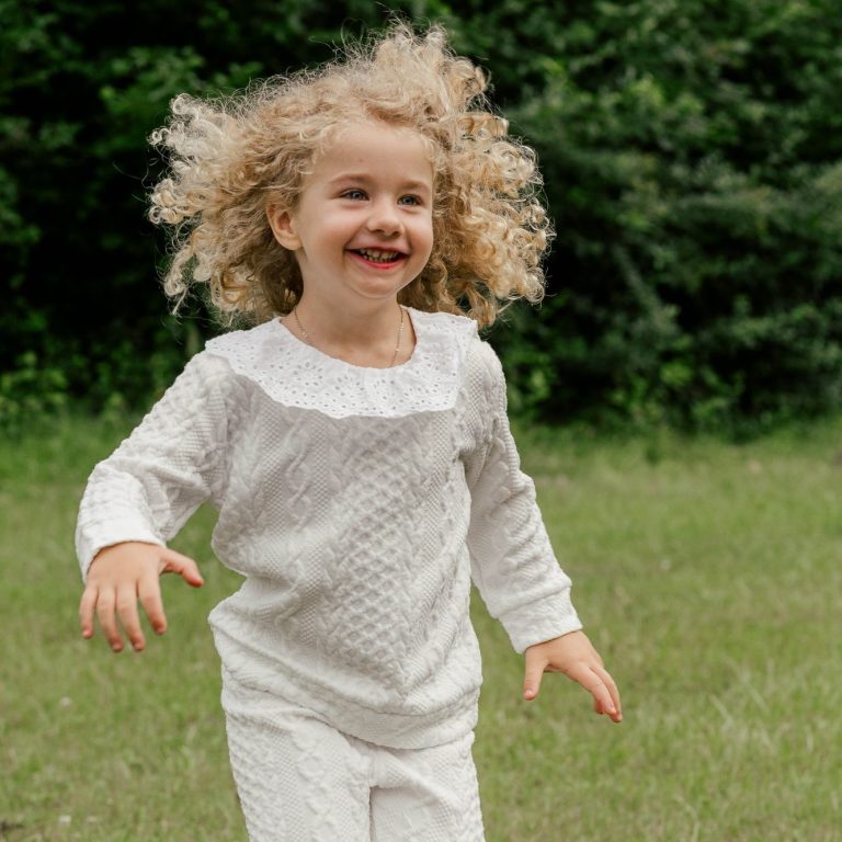 Familienfotografie mit Spaß und Leichtigkeit Ein fröhliches Kind mit lockigem Haar, das in einem grünen Feld läuft.